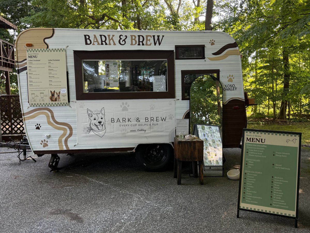 The Bark & Brew camper trailer from the side, with menu boards and a mirror beside it