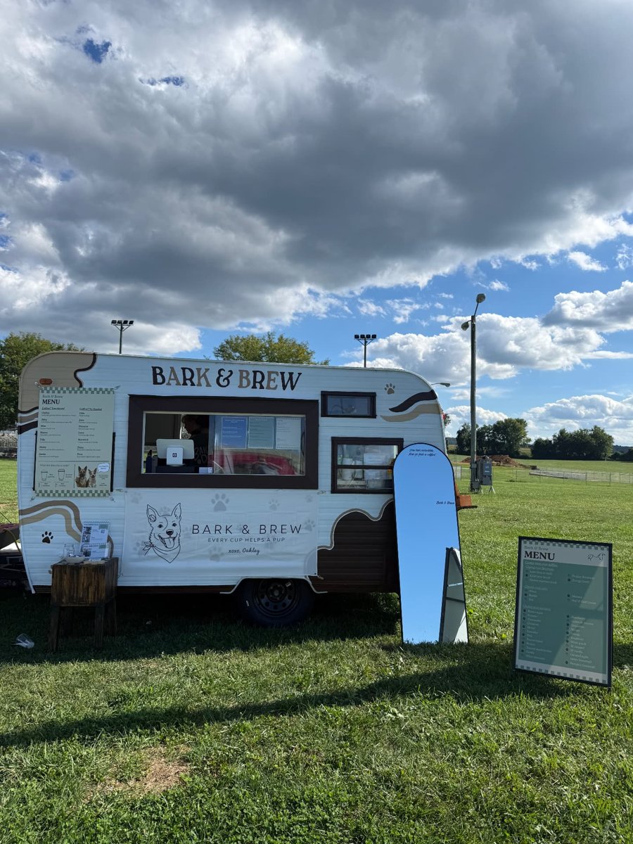 The Bark & Brew trailer set up in an open field with its menu boards and a standing mirror