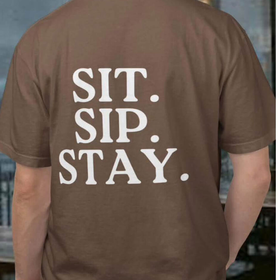 Brown t-shirt with a small Bark & Brew chest print and “Sit. Sip. Stay.” on the back