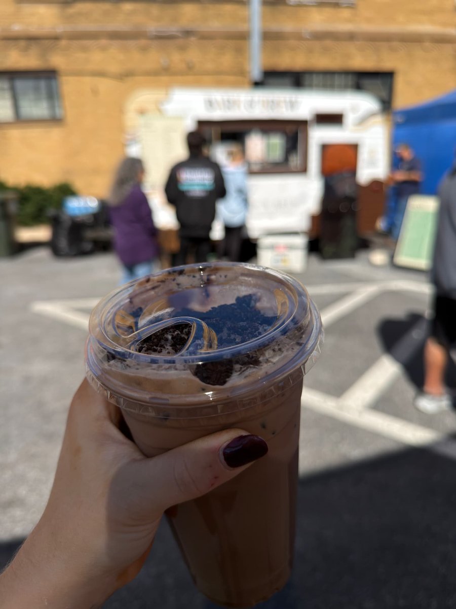 An iced drink topped with crushed cookies held up while the Bark & Brew trailer serves a line of people behind it