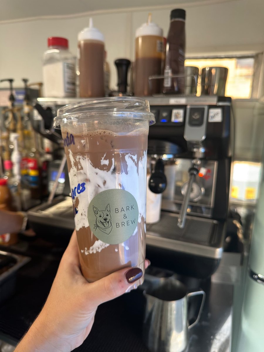A Bark & Brew iced coffee held in front of the espresso machine inside the trailer